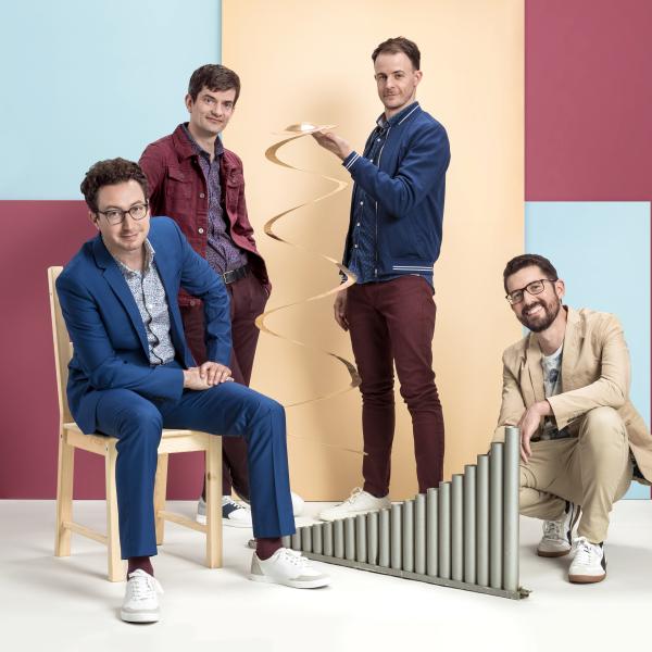 Third Coast Percussion – four young men stand at various heights wearing blue, maroon, and tan in front of a backdrop of light blue, mauve, and tan squares, holding percussion instruments